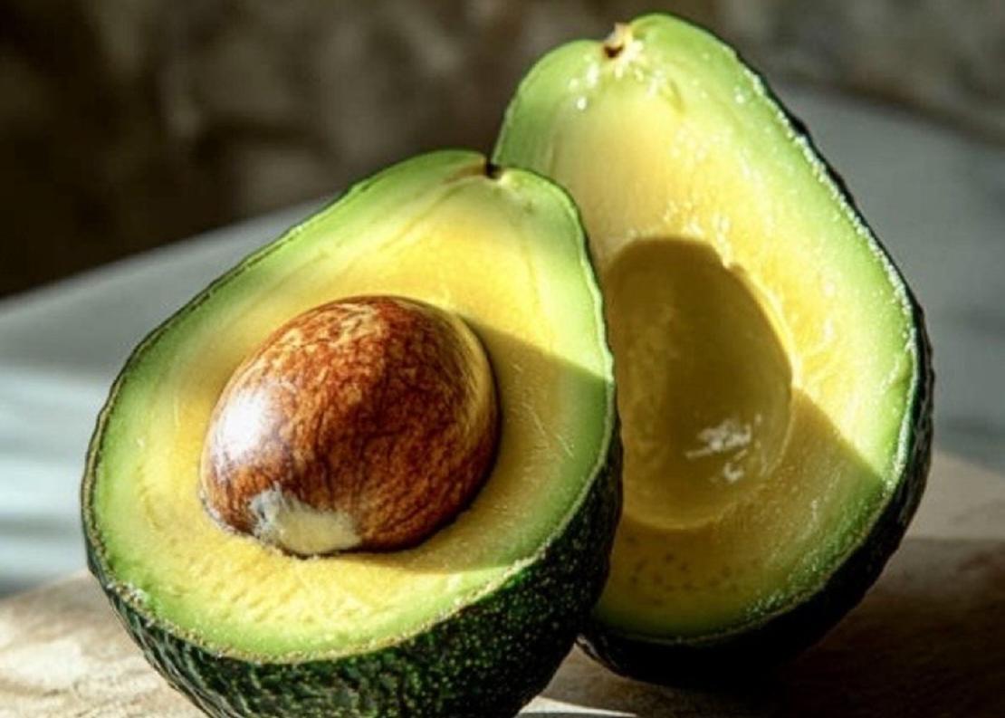 An avocado cleanly cut in half, displaying both halves with the pit still intact.