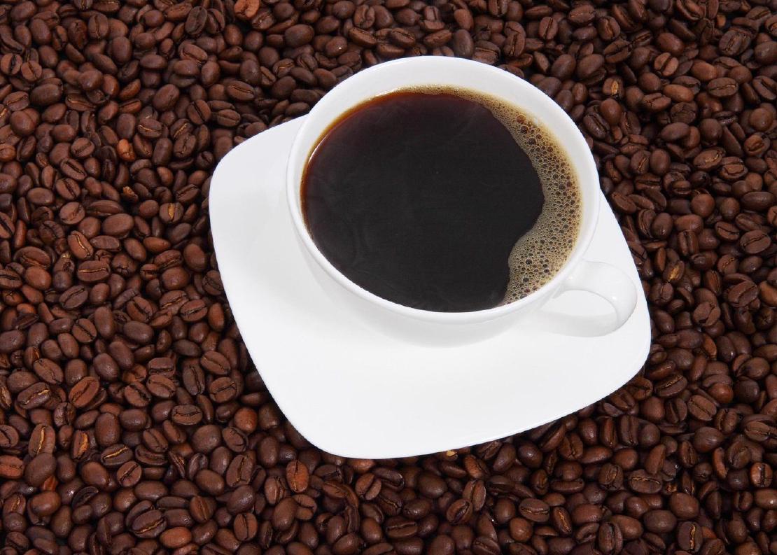 A cup of coffee on a field of coffee beans.