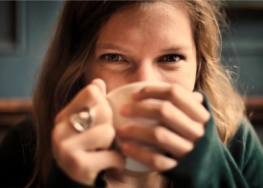 A young woman really enjoying a cup of coffee, holding it with both hands.