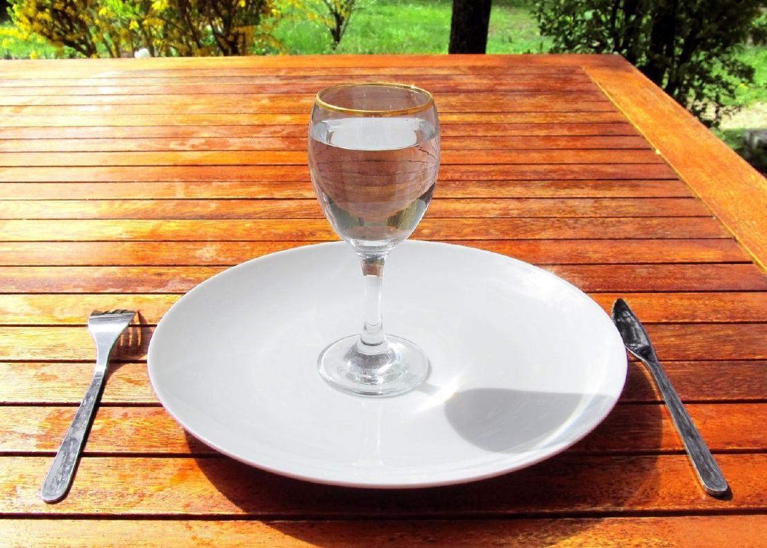 A glass of water sitting in the center of an empty plate with a knife on one side and a fork on the other.
