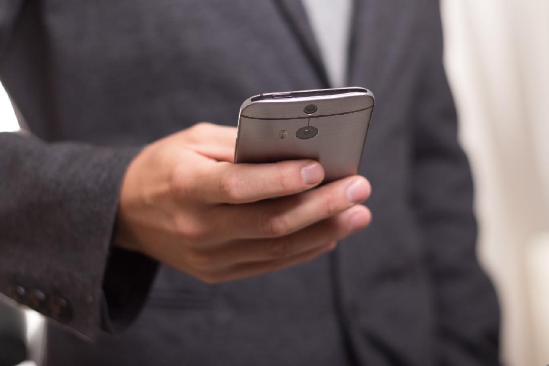 A man in a dark suit coat is holding a smartphone in his hand.