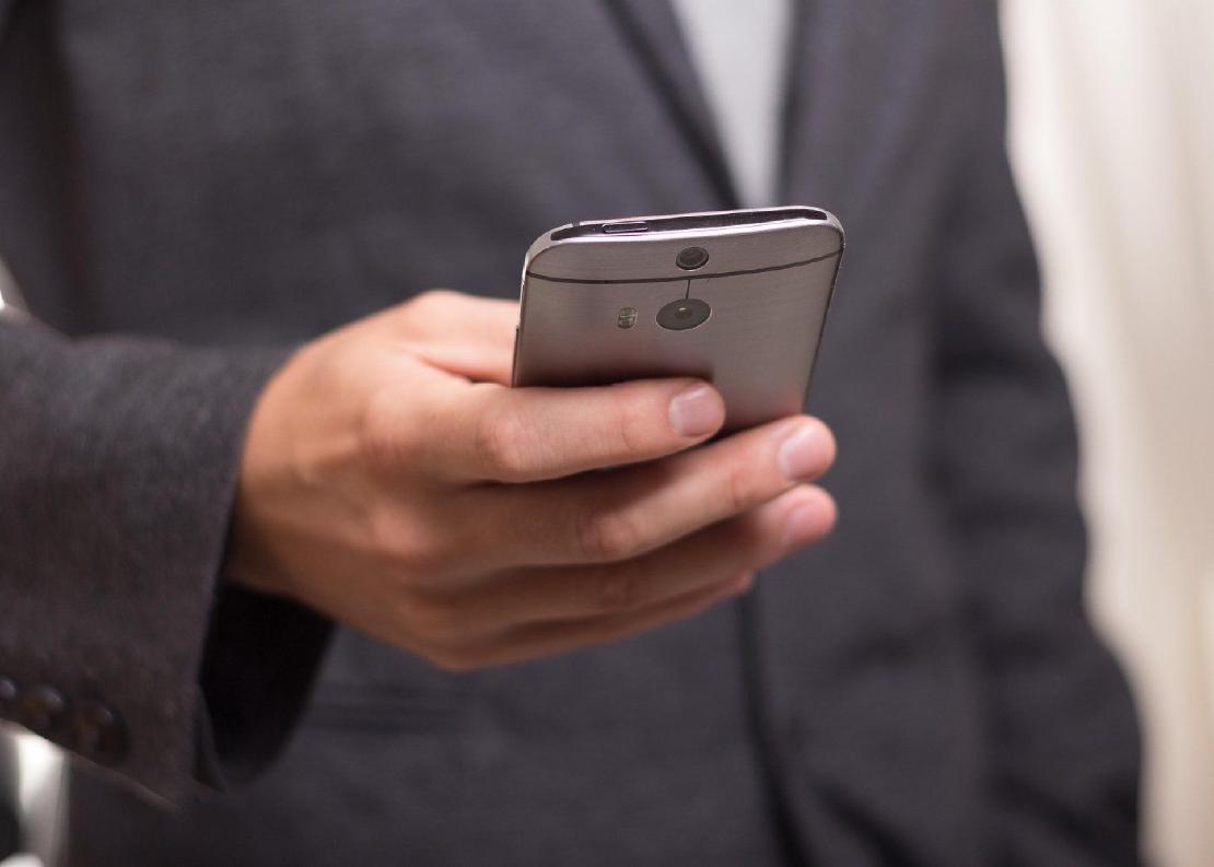 A man in a dark suit coat is holding a smartphone in his hand.