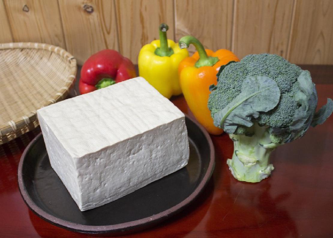 A whole block of white tofu sitting on a plate surrounded by vegetables.