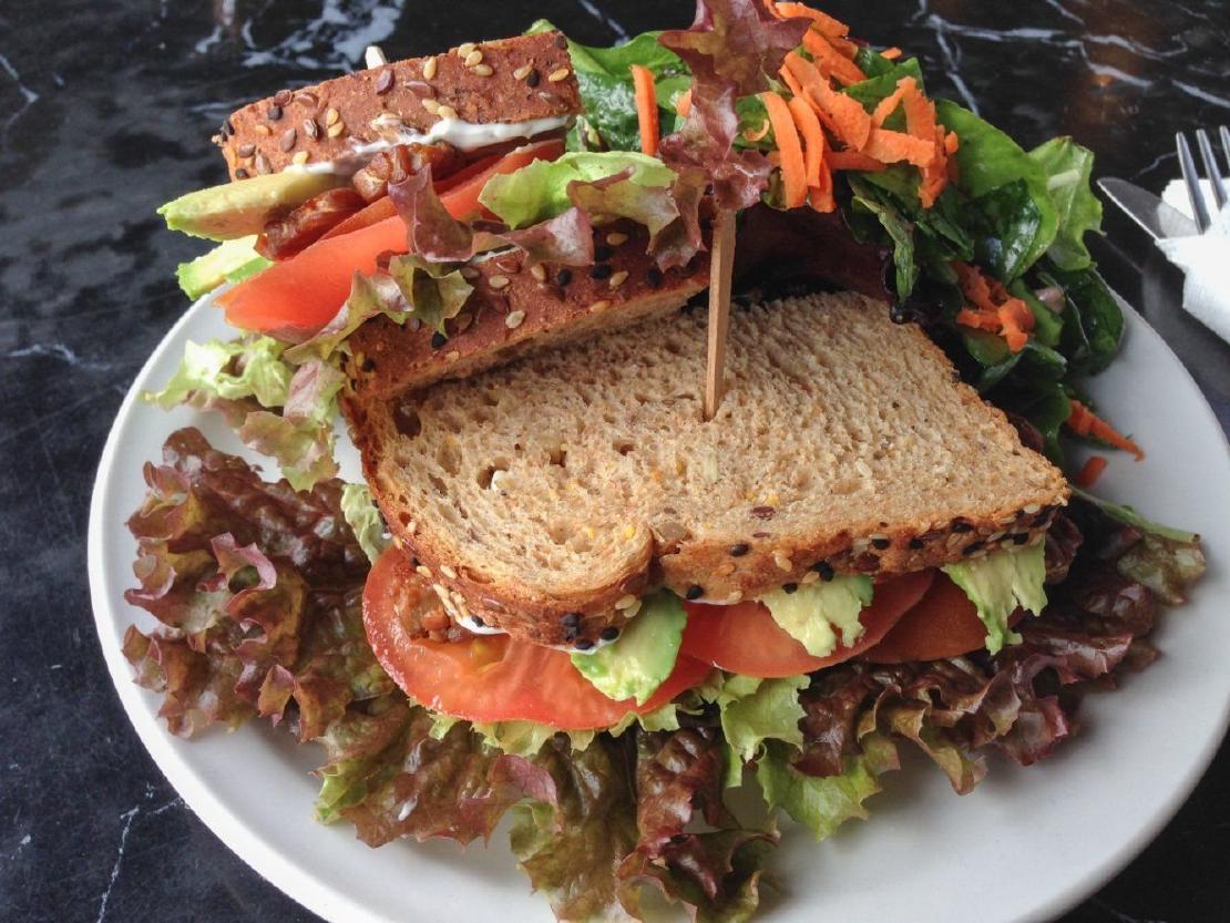A vegan BLT on whole wheat bread sitting on a white plate.