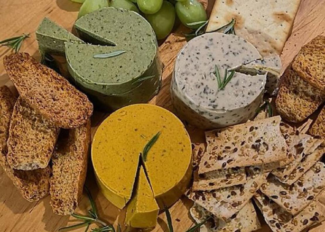 A board with an assortment of vegan cheeses, crackers and bread with a garnish of rosemary.