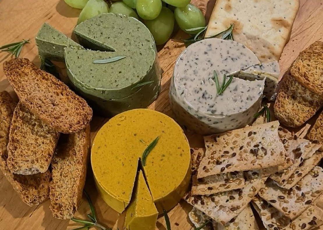 A board with an assortment of vegan cheeses, crackers and bread with a garnish of rosemary.