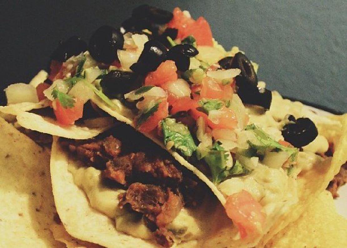 A close-up image of vegan nachos with tortilla chips, tomatoes, onions, plant-based meat and cheese, and black olives.